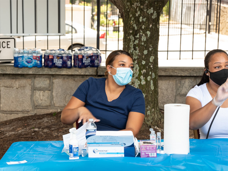 Two women sitting at a table with hand sanitizer and other clearning products to give away.